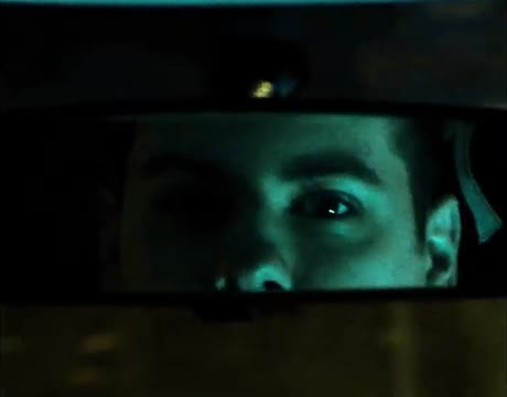A man's eyes in a car's rear-view mirror at night